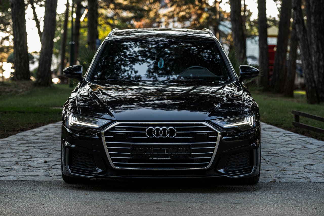 Luxury black car parked on a path in a tranquil forest setting, showcasing modern elegance.